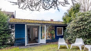 A small blue house with a tiled roof, a glass door entrance, and a patio with two white plastic chairs. - Chalet 'Hochwald' with Shared Terrace, Private Garden and Wi-Fi (Bad Sachsa)