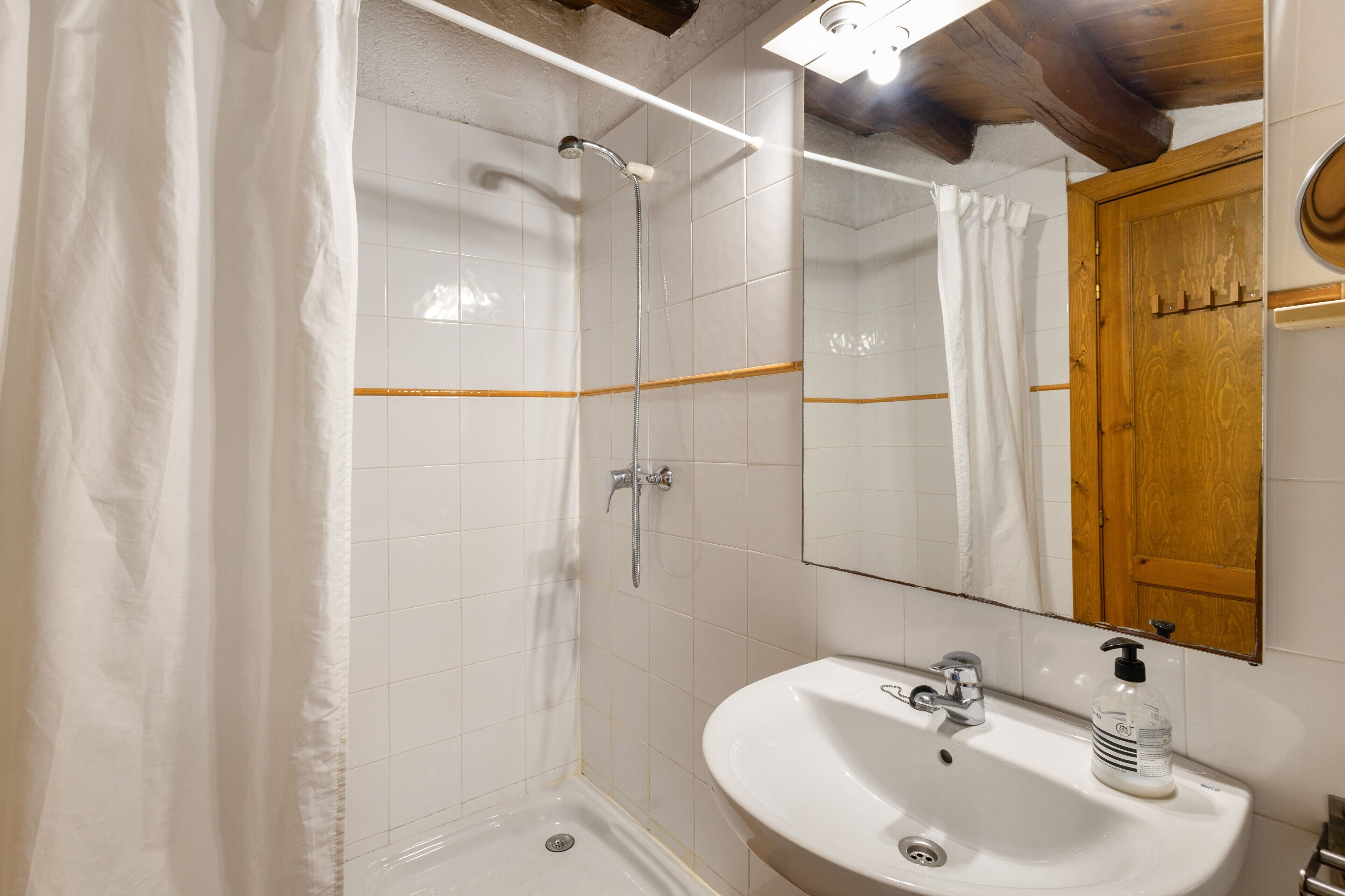 Une salle de bain avec une douche, un lavabo, un miroir et une porte en bois.