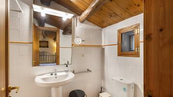 Une salle de bain avec un lavabo, des toilettes et un miroir, le tout de couleur blanche.