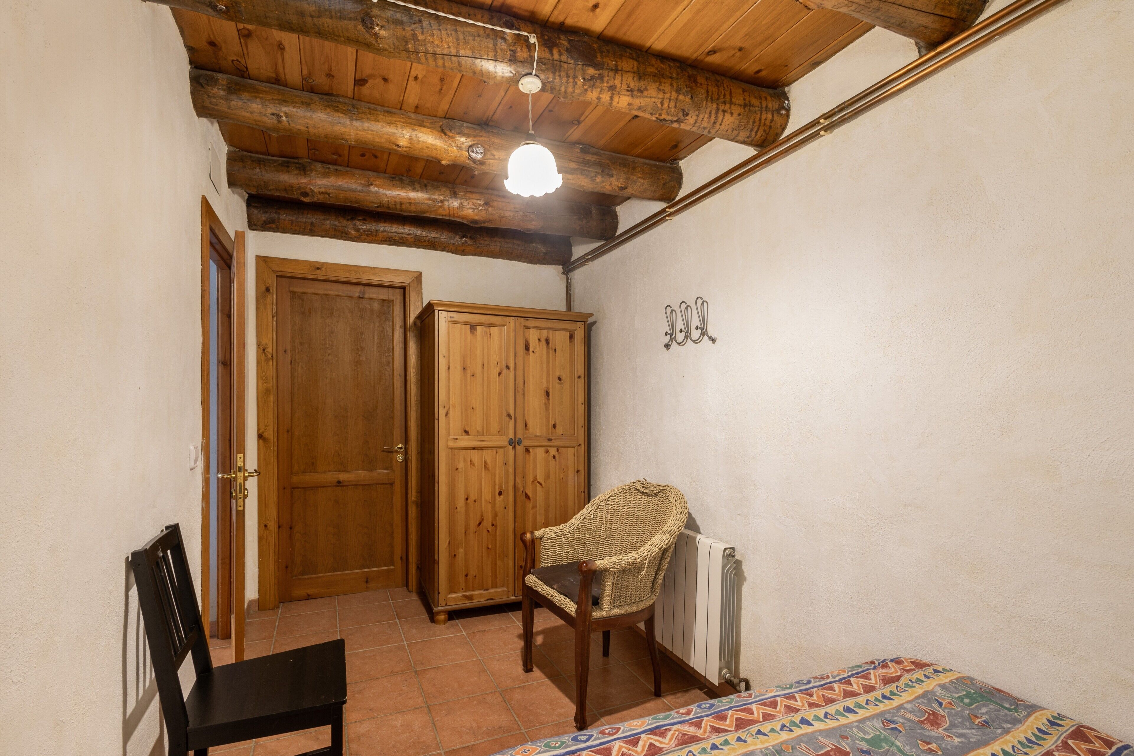A room with a wooden ceiling, a chair, a bed, a wardrobe, and a radiator.