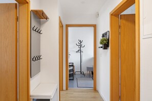 Un pasillo con puertas de madera, un perchero, una mesita y una planta.