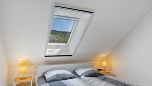 A bedroom with a skylight, two bedside tables with lamps, a bed with striped bedding, and a view of greenery outside. - Holiday Apartment 'Kleinbreitenbach 2' with Mountain View and Wi-Fi (Plaue)
