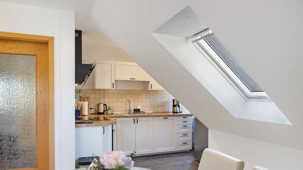 A modern kitchen with white cabinets, a skylight, and a dining area with a table and chairs. - Holiday Apartment 'Kleinbreitenbach 2' with Mountain View and Wi-Fi (Plaue)