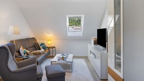 A modern living room with a sofa, armchair, coffee table, TV, and a small window. - Holiday Apartment 'Kleinbreitenbach 2' with Mountain View and Wi-Fi (Plaue)