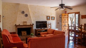 A living room with a fireplace, television, orange sofas, and a ceiling fan.