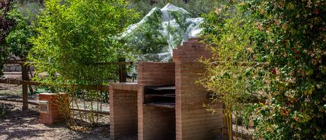 A brick-built outdoor structure with a transparent cover, surrounded by greenery and a brick wall.