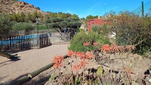 A fenced garden area with a pool, a wooden deck, and a red building in the background.