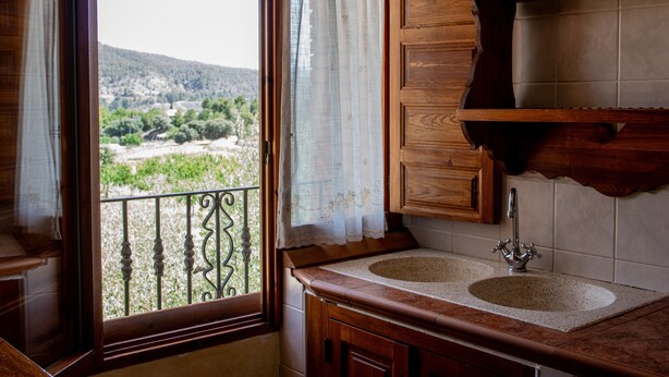 A kitchen with two sinks, wooden cabinets, and a view of a mountainous landscape through a window.