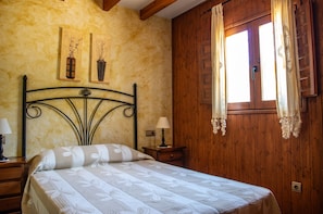 A bedroom with a bed, wooden walls, a window with curtains, and two wall-mounted lamps.