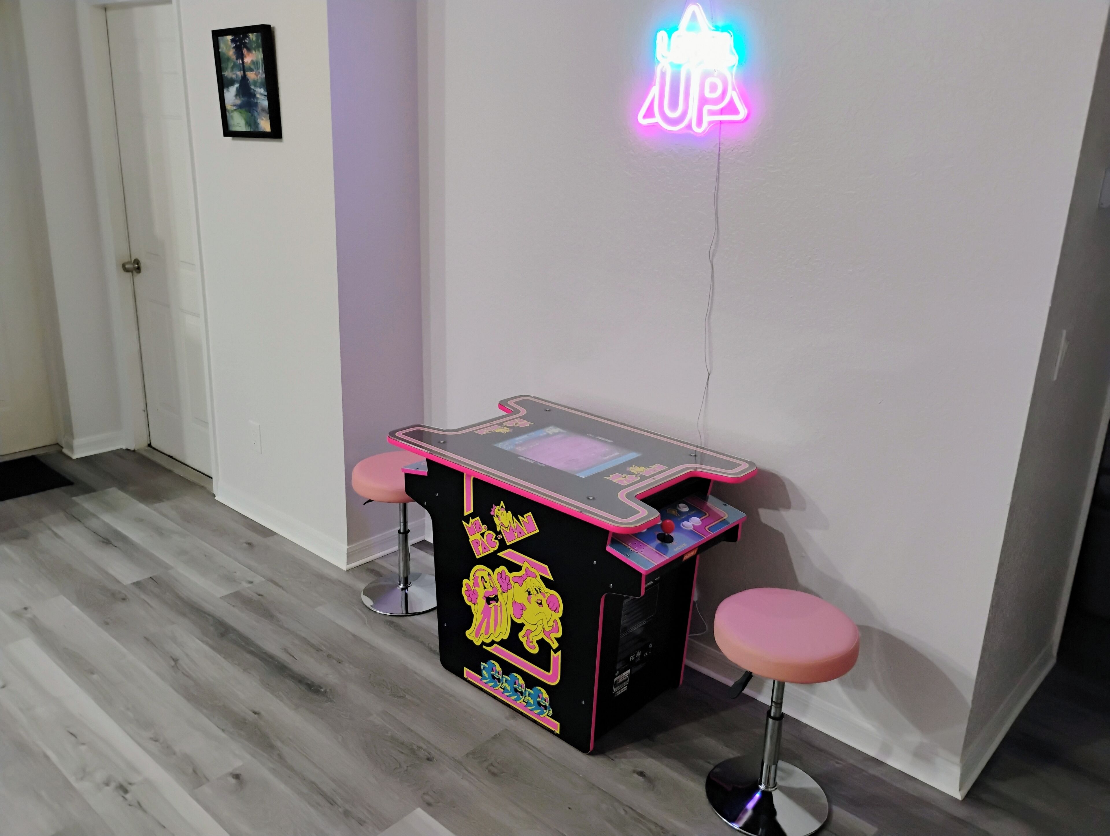 A room with a neon sign, a gaming table, and two stools.