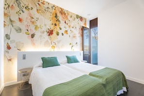 Une chambre d’hôtel avec deux lits, une décoration murale à motifs floraux et une vue à travers une porte vitrée.