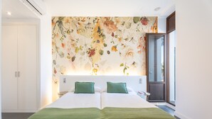 Une chambre avec un grand décor mural représentant des motifs floraux, une couvre-lit verte et une table de chevet.