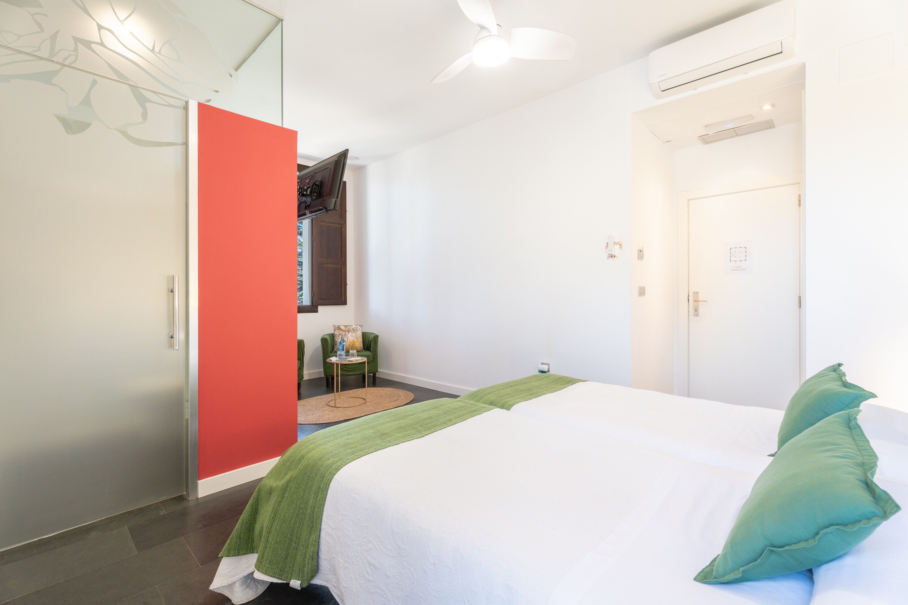 Une chambre avec un lit, un oreiller vert, un paravent rouge, une petite table avec une chaise et un appareil de climatisation.
