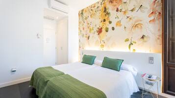 A hotel room with a large floral mural, a bed with green bedding, a bedside table with a phone, and a door.