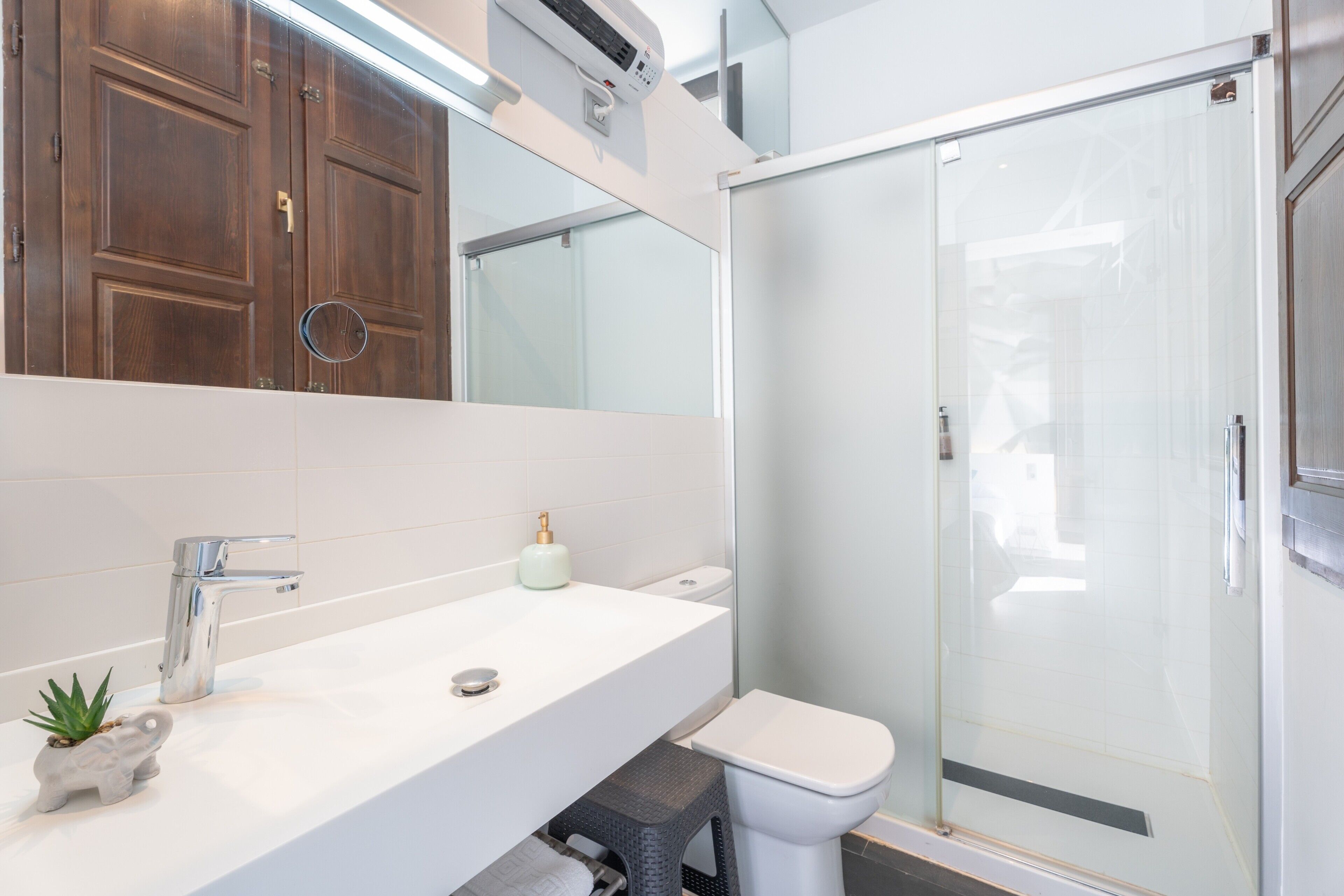 Un baño con un lavamanos blanco, un inodoro, una cabina de ducha de cristal y un mueble de tocador de madera con un espejo.