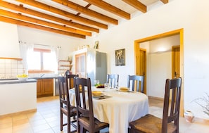 A dining area with a round table, chairs, and a kitchen in the background.