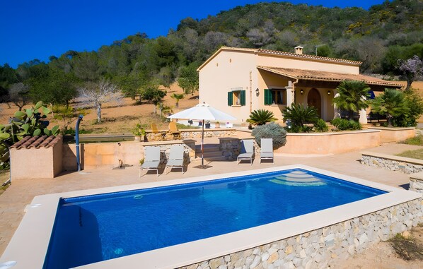 A pool with lounge chairs, a patio area, and a house with a tiled roof.