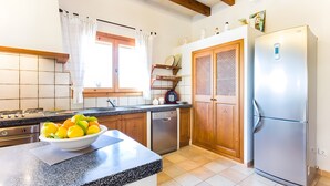 Une cuisine dotée d’un plan de travail en granit, d’un réfrigérateur en acier inoxydable, de meubles en bois et d’une fenêtre agrémentée de rideaux blancs.