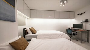Un dormitorio moderno con dos camas, un escritorio con computadora y un televisor montado en la pared.