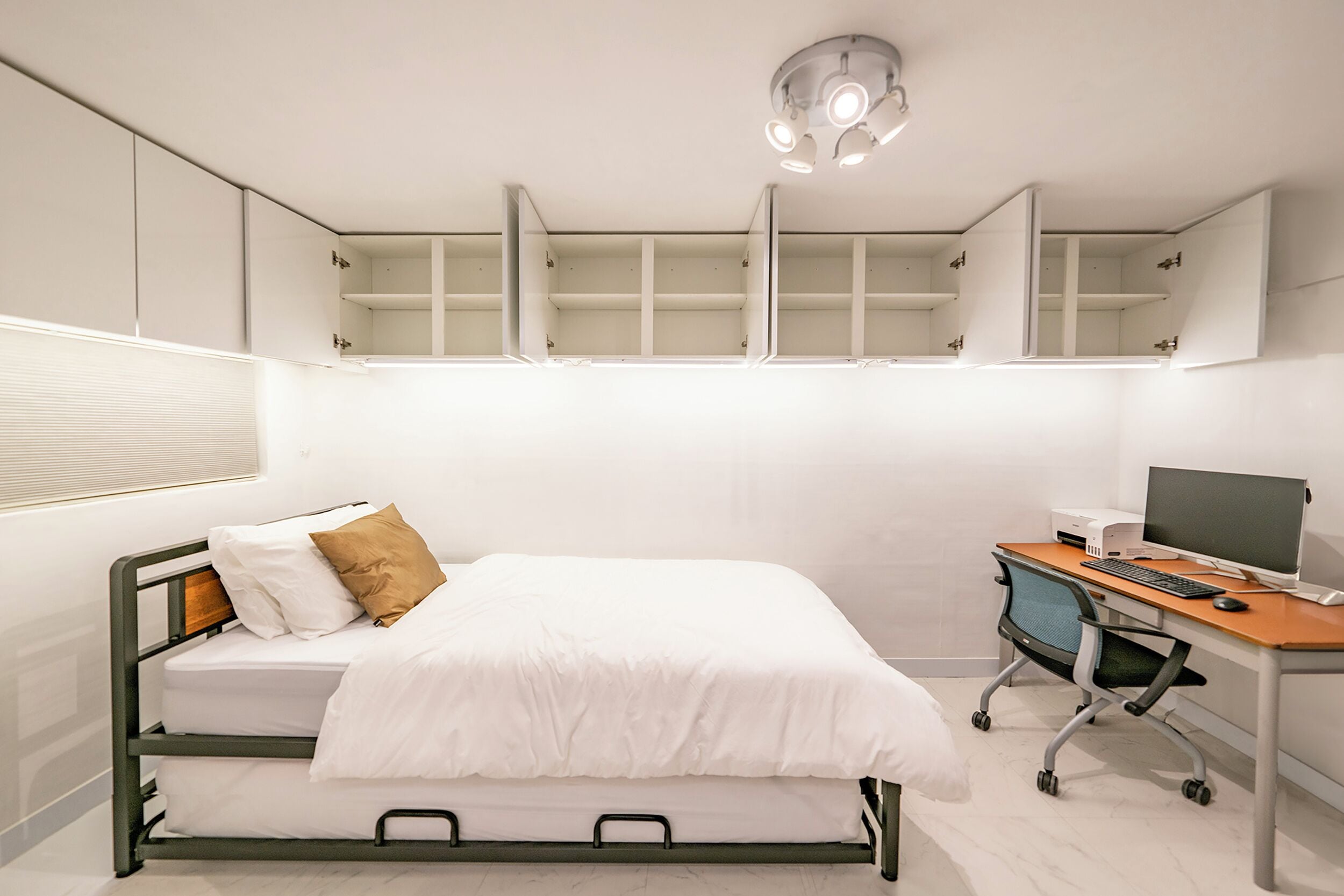 A bedroom with a bed, a desk with a computer, and built-in shelving above the bed.