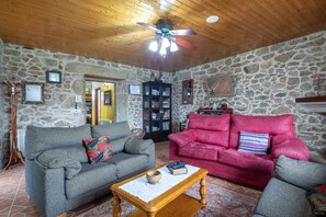 A living room with stone walls, wooden ceiling, two sofas, a coffee table, and a ceiling fan. - Apartment 'Casa Rural Os Carballos' with Private Pool, Wi-Fi and Air Conditioning (Pontevedra)