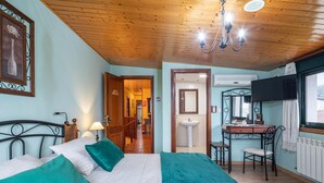 A bedroom with a bed, a desk, a chair, a TV, and a bathroom. - Apartment 'Casa Rural Os Carballos' with Private Pool, Wi-Fi and Air Conditioning (Pontevedra)