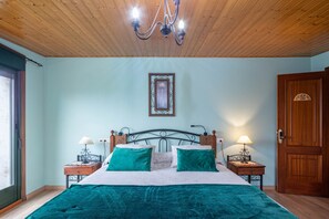 A bedroom with a wooden ceiling, a bed with green bedding, two bedside tables with lamps, and a door with a sign. - Apartment 'Casa Rural Os Carballos' with Private Pool, Wi-Fi and Air Conditioning (Pontevedra)