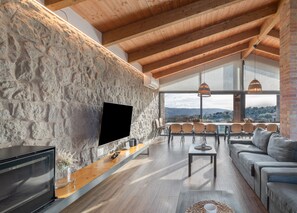 A spacious living area with a stone wall, a flat-screen TV, wooden ceiling beams, a dining table with chairs, and a sofa. - Country House 'El Salvans' with Mountain View, Wi-Fi and Air Conditioning (Sagas)