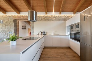 Eine moderne Küche mit weißen Schränken, einer Steinwand, Holzbalken und Edelstahlgeräten.