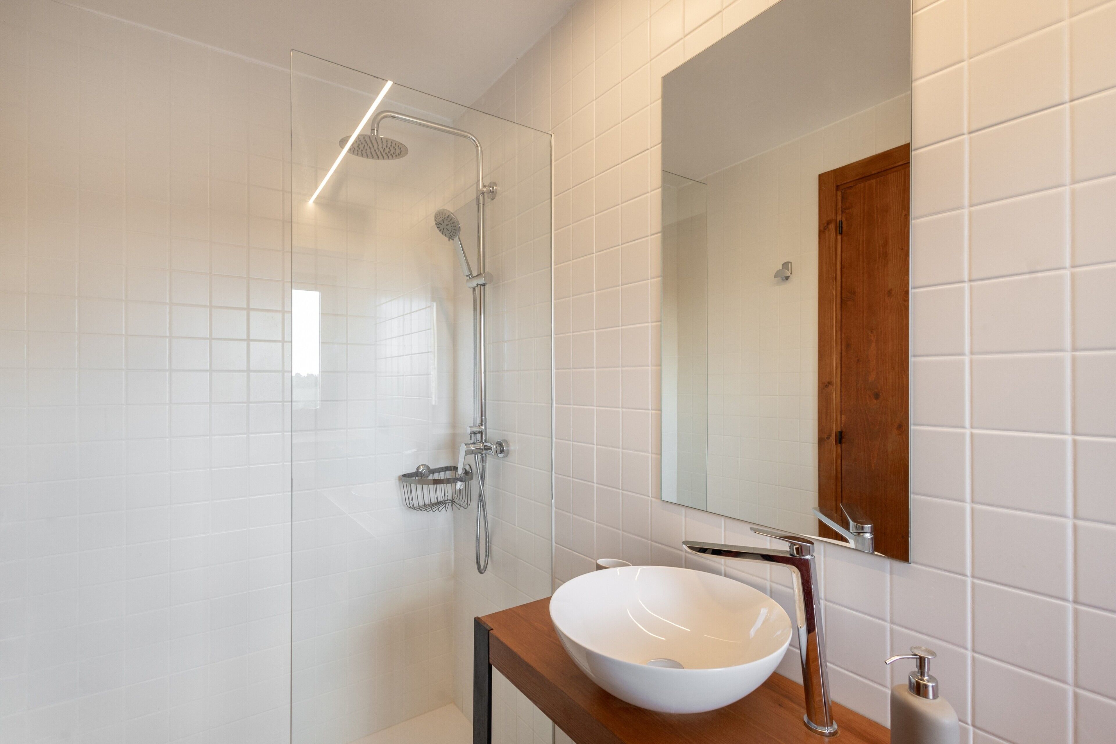 Un baño moderno con cabina de ducha de vidrio, lavabo blanco y tocador de madera.