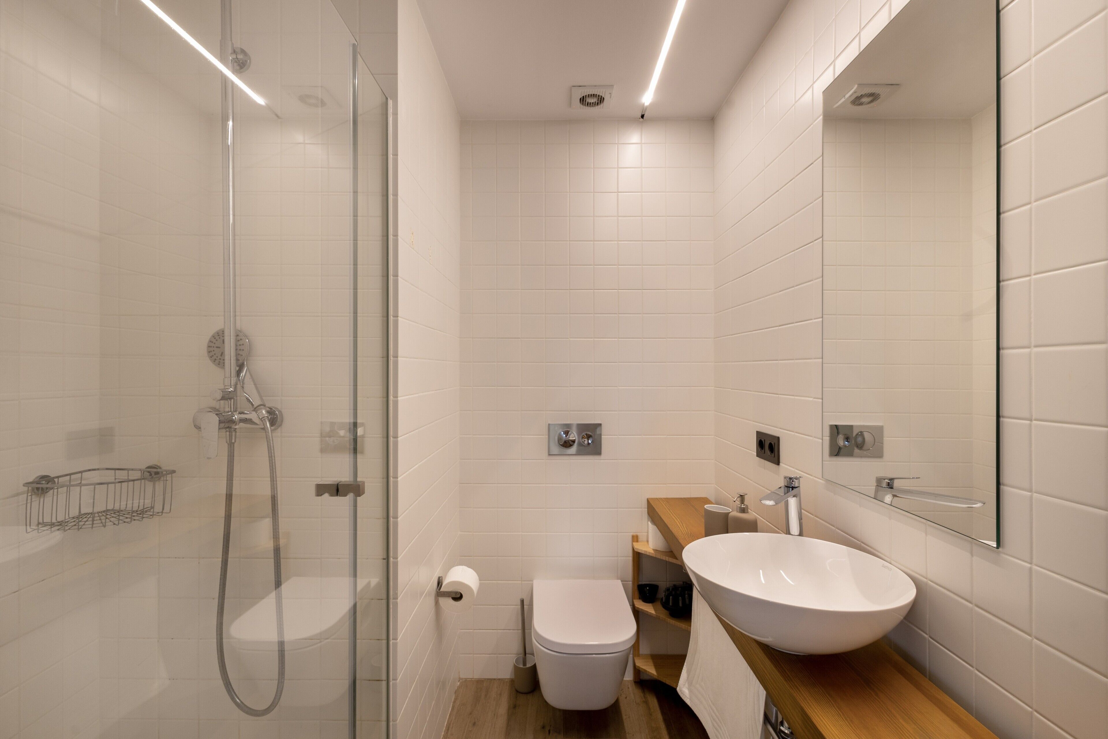 Een moderne badkamer met een douchecabine van glas, een wit toilet en een houten wastafelmeubel met een witte wastafel.