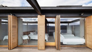 Un dormitorio moderno con puertas de vidrio, suelo de madera y vistas a la montaña.
