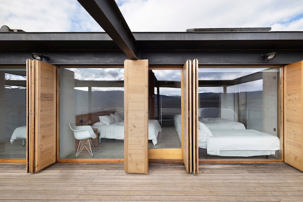 A modern bedroom with glass doors, wooden flooring, and a view of the mountains.