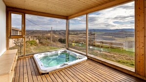 Una terraza de madera con jacuzzi, amplias ventanas y vistas al campo.