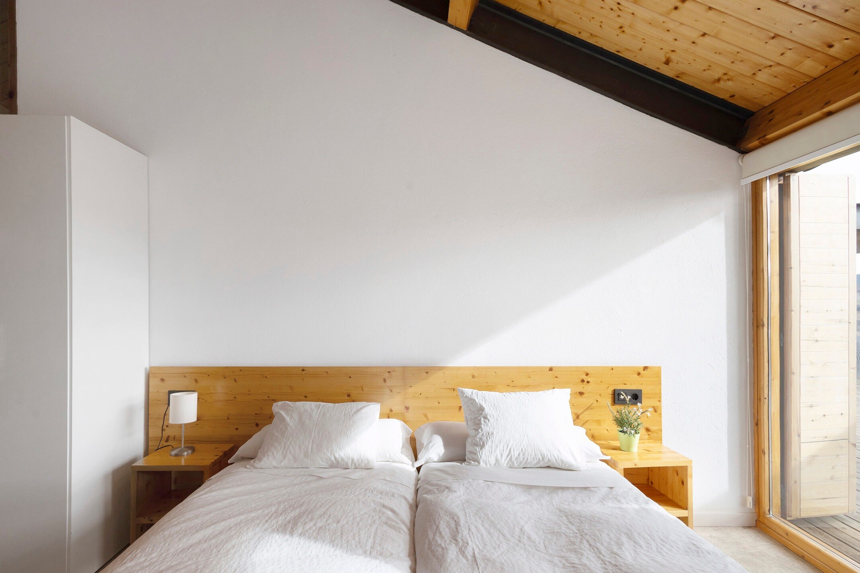 A bedroom with a wooden headboard, two beds, a nightstand with a lamp, and a window.