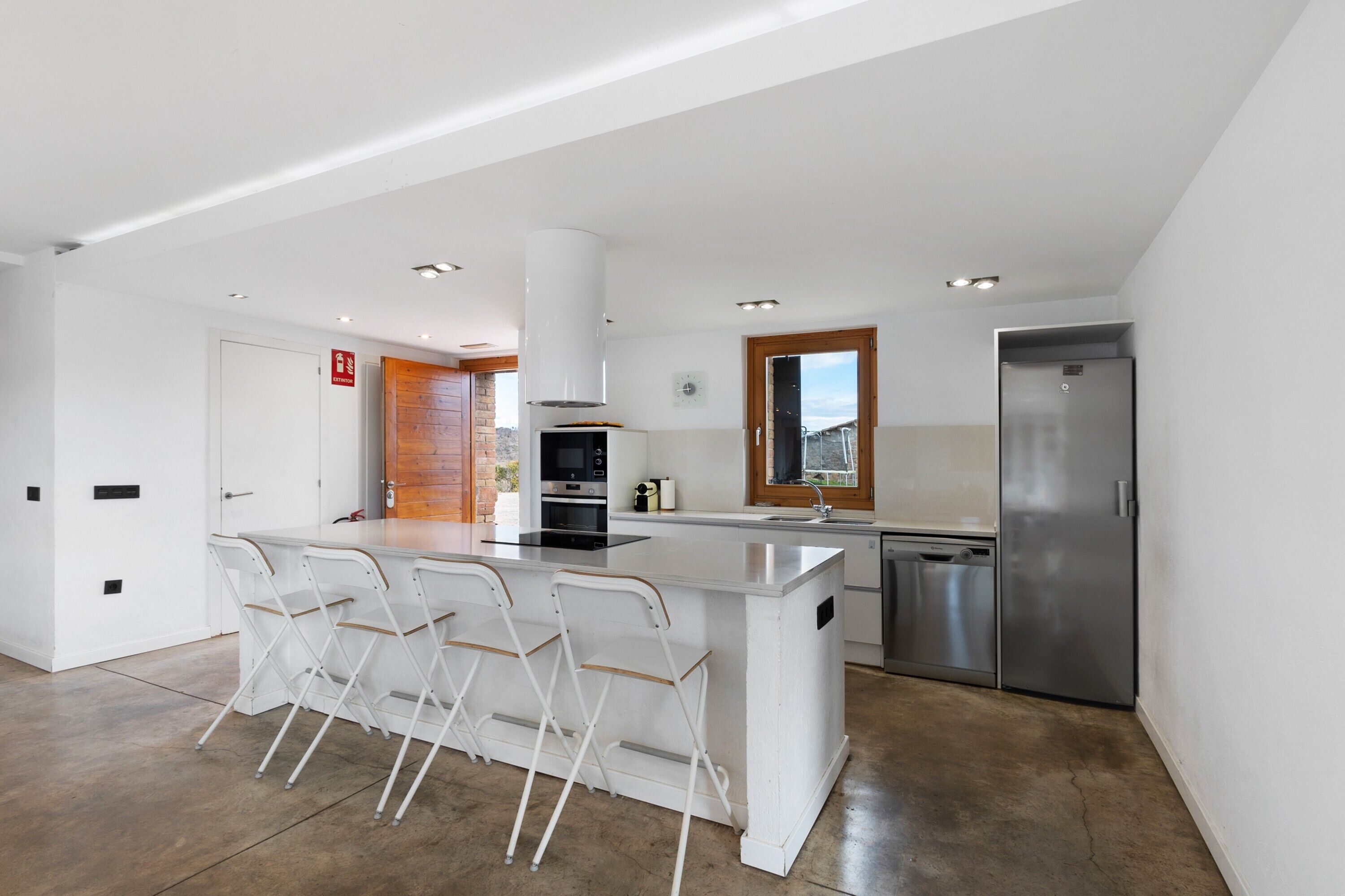 Una cocina moderna con una isla central, taburetes de bar, un refrigerador de acero inoxidable y un revestimiento de pared de madera.
