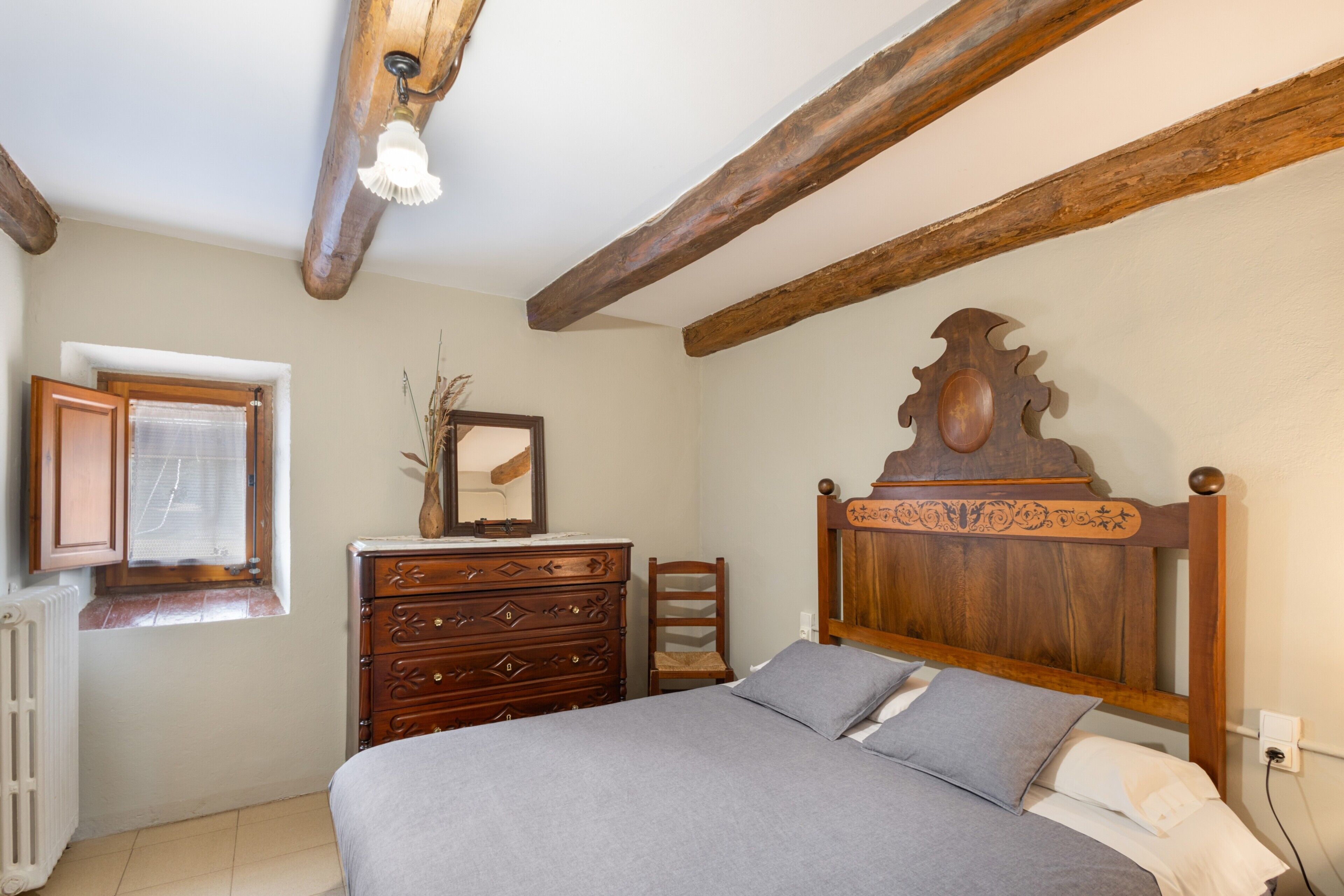 Un dormitorio con cabecera de madera, cómoda, silla y ventana con vistas.