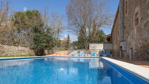 A swimming pool with blue tiles, surrounded by trees and a stone building.