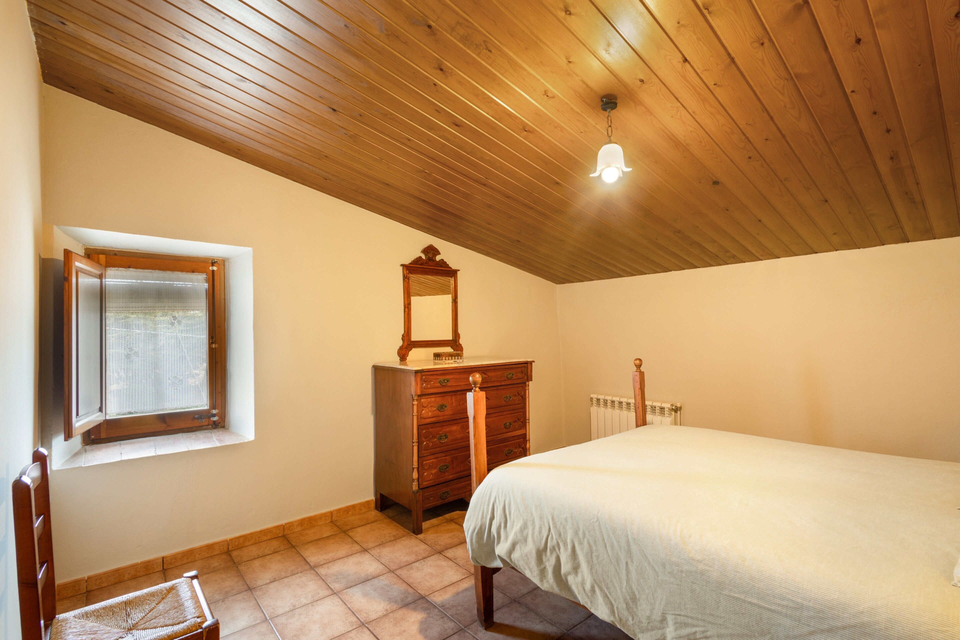 Une chambre avec un plafond en bois, un lit, une commode, un miroir et une fenêtre.