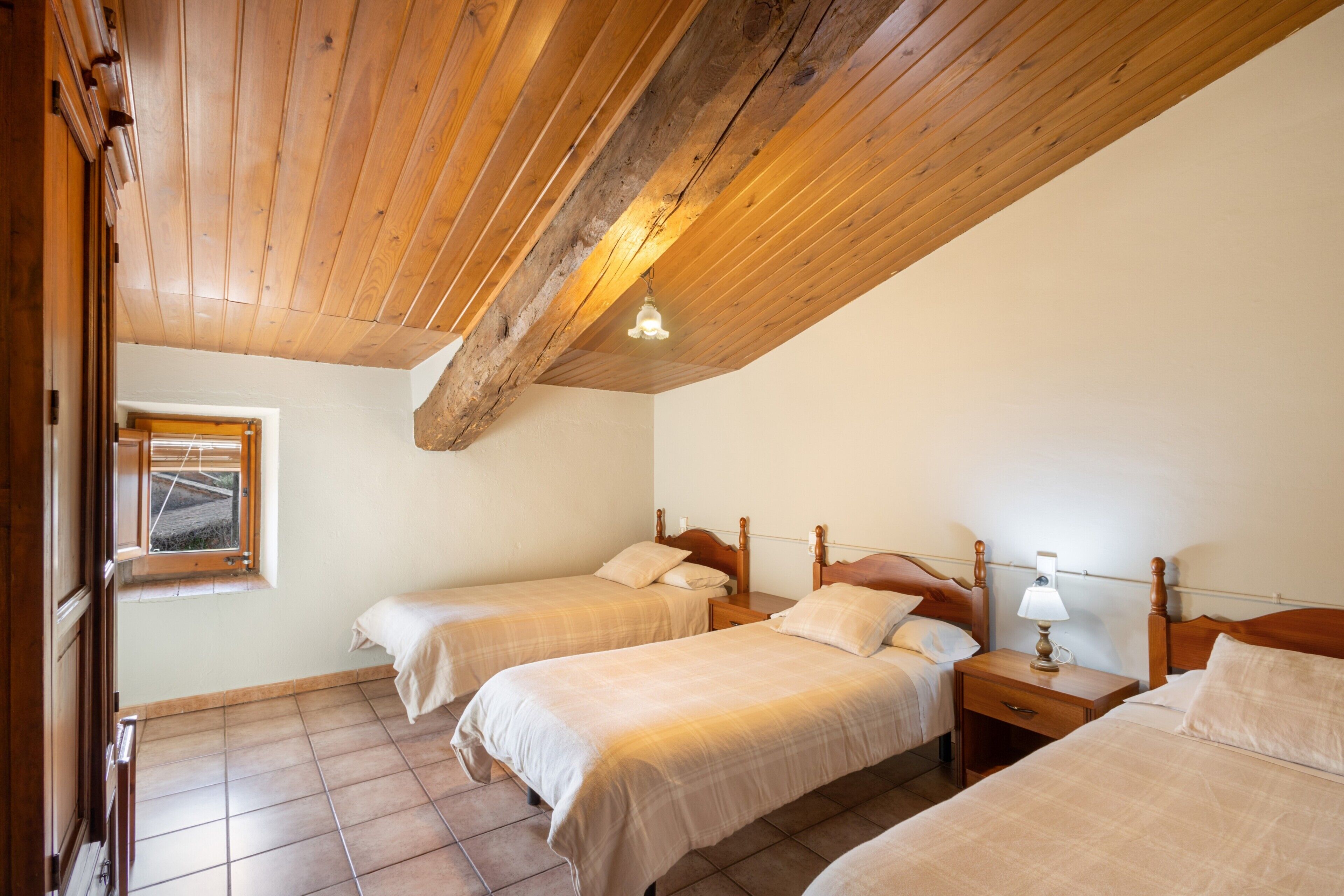 Un dormitorio con dos camas, cabeceros de madera, una ventana y techo de madera.