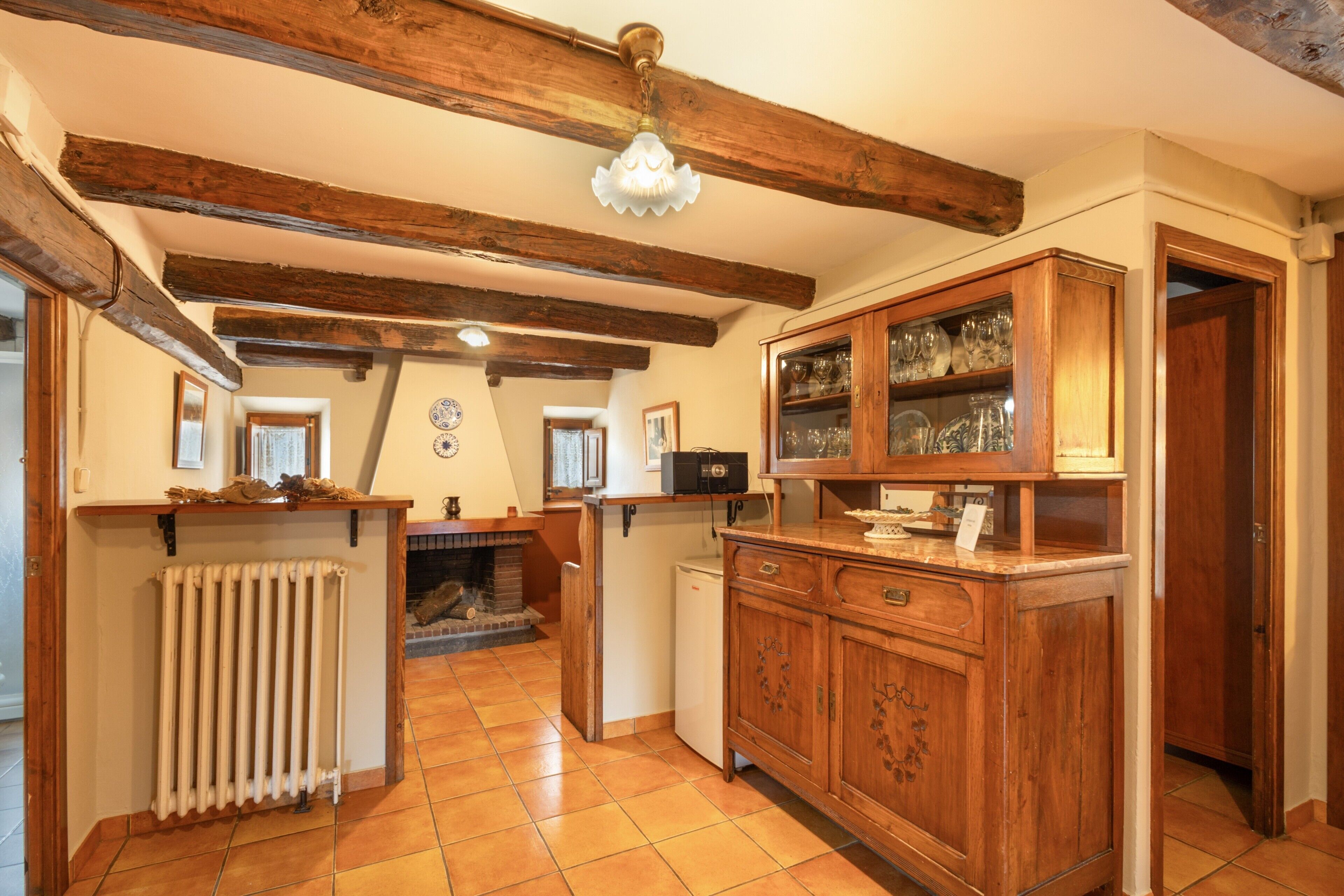 Une cuisine avec des poutres en bois, un radiateur, un réfrigérateur et des meubles de rangement en bois dotés de portes en verre.