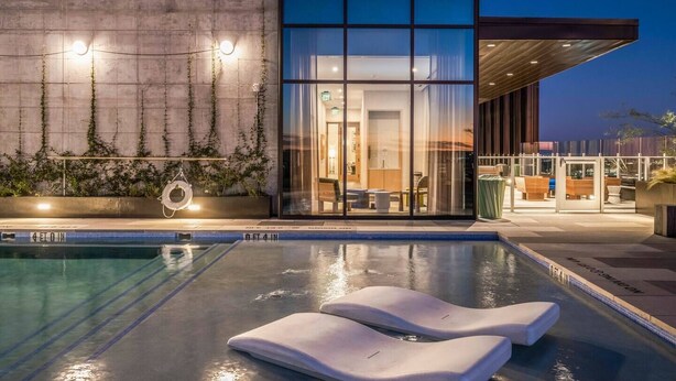 Un hôtel moderne doté d'une piscine, de portes vitrées et d'un espace extérieur aménagé pour s'asseoir.