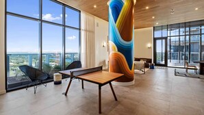 Une pièce spacieuse avec de grandes fenêtres, une table en bois et un pilier abstrait aux couleurs vives.