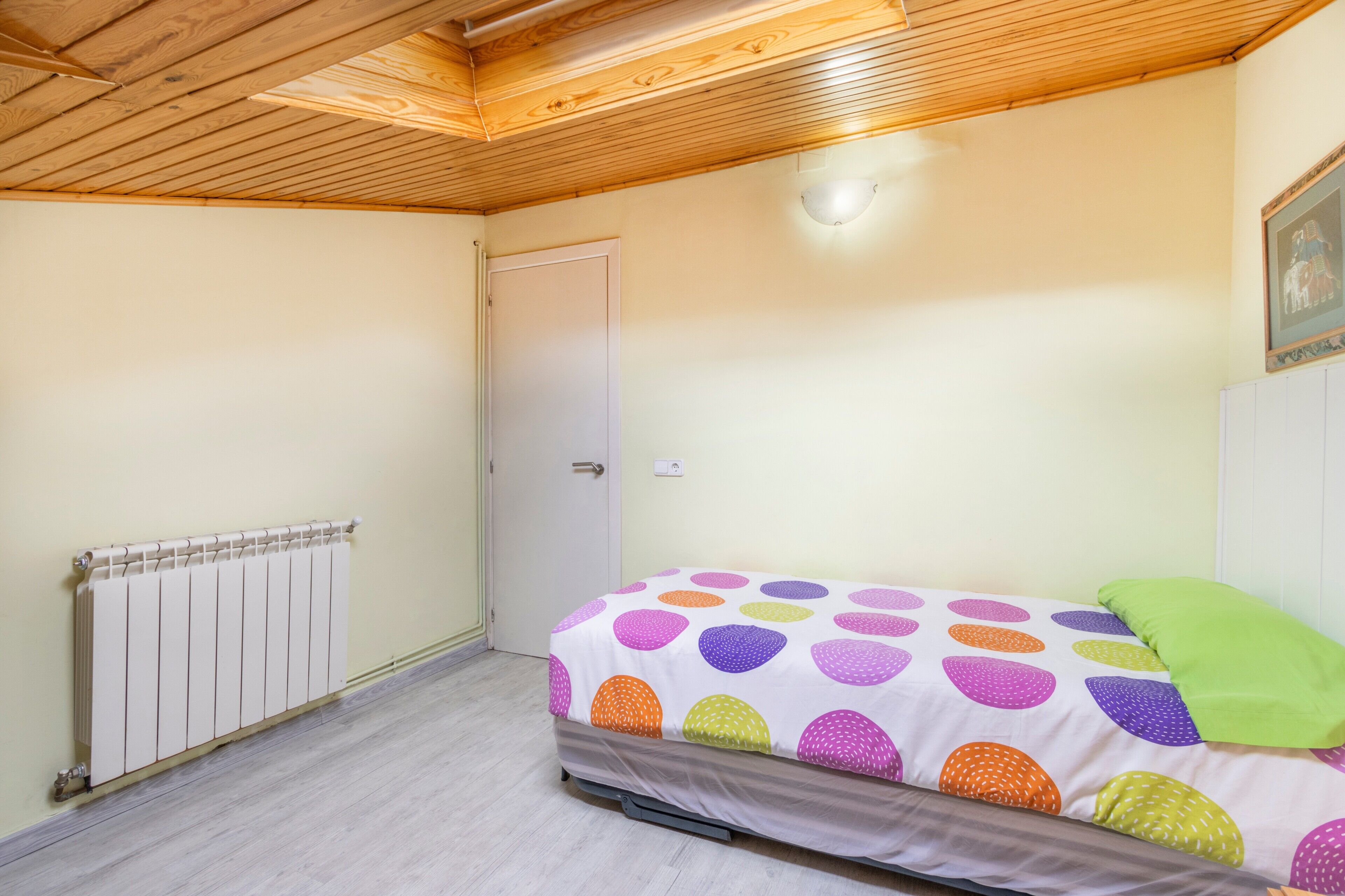A bedroom with a bed, a radiator, a door, and a wooden ceiling.