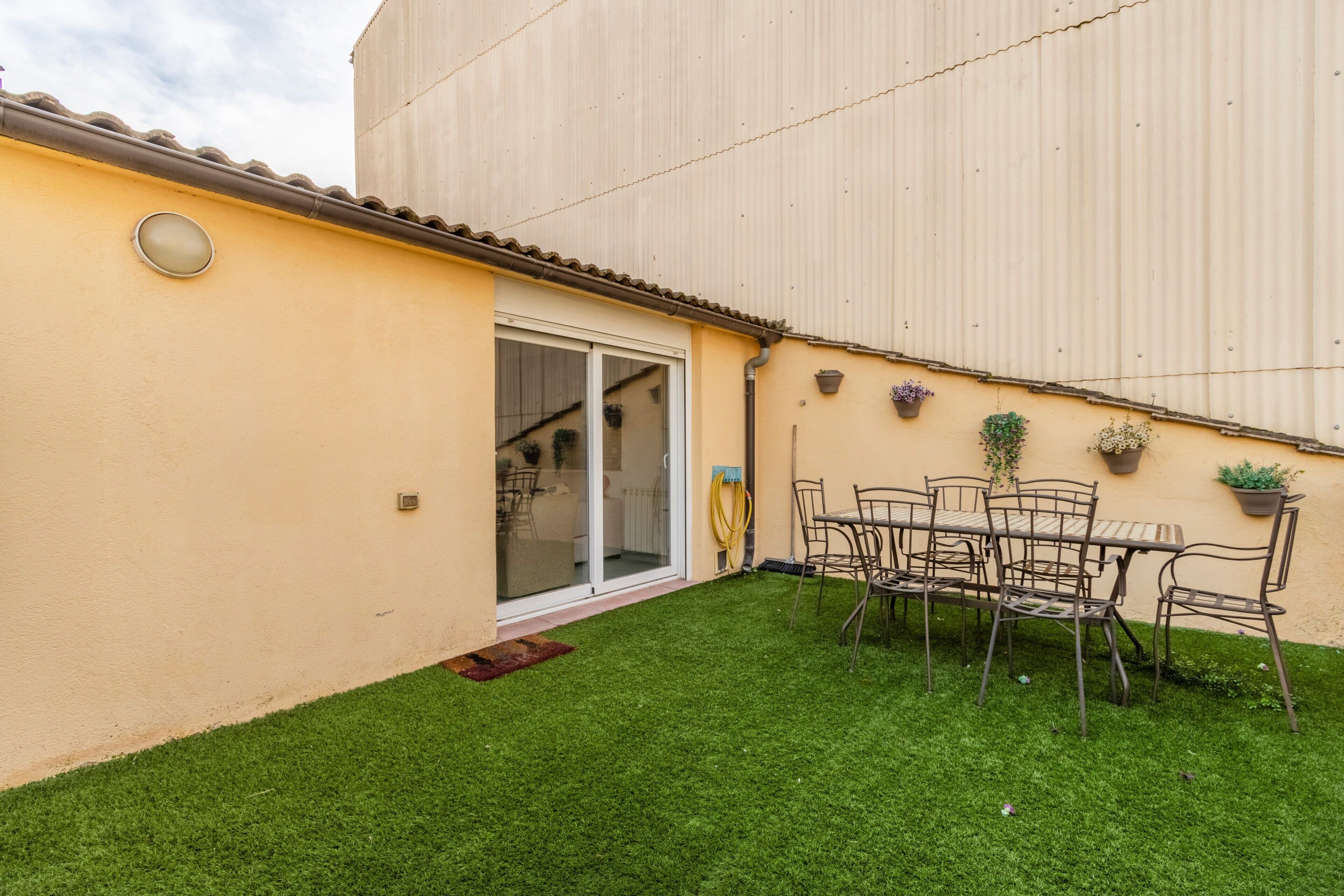 A patio with a table and chairs, a sliding glass door, and potted plants.