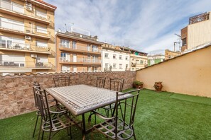 A rooftop terrace with a table and chairs, a stone wall, and a view of surrounding buildings.
