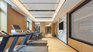 A gym with treadmills lined up against a wall with a large screen displaying a presentation. - Fairfield by Marriott Haikou Meilan (Haikou)