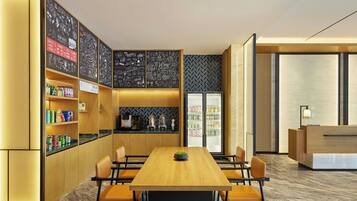 Un moderno hall de hotel con un mostrador de recepción, una larga mesa de madera con sillas, una zona de cocina con estantes llenos de bebidas y una pared con diseño.