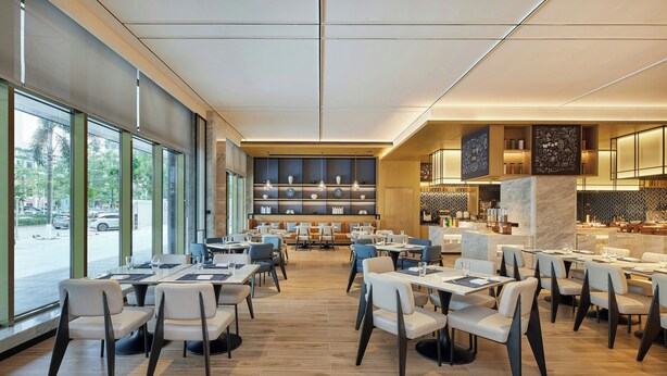 A modern restaurant with a long dining area, large windows, and a central bar area. - Fairfield by Marriott Haikou Meilan (Haikou)