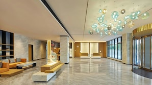 A spacious lobby with a modern design, featuring a seating area with sofas and a coffee table, a marble floor, and a unique ceiling light fixture. - Fairfield by Marriott Haikou Meilan (Haikou)